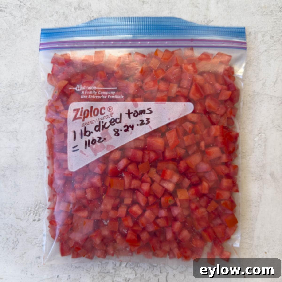 A clear zip-top freezer bag filled with perfectly diced fresh tomatoes, flattened and ready for freezing, showcasing organized food storage.