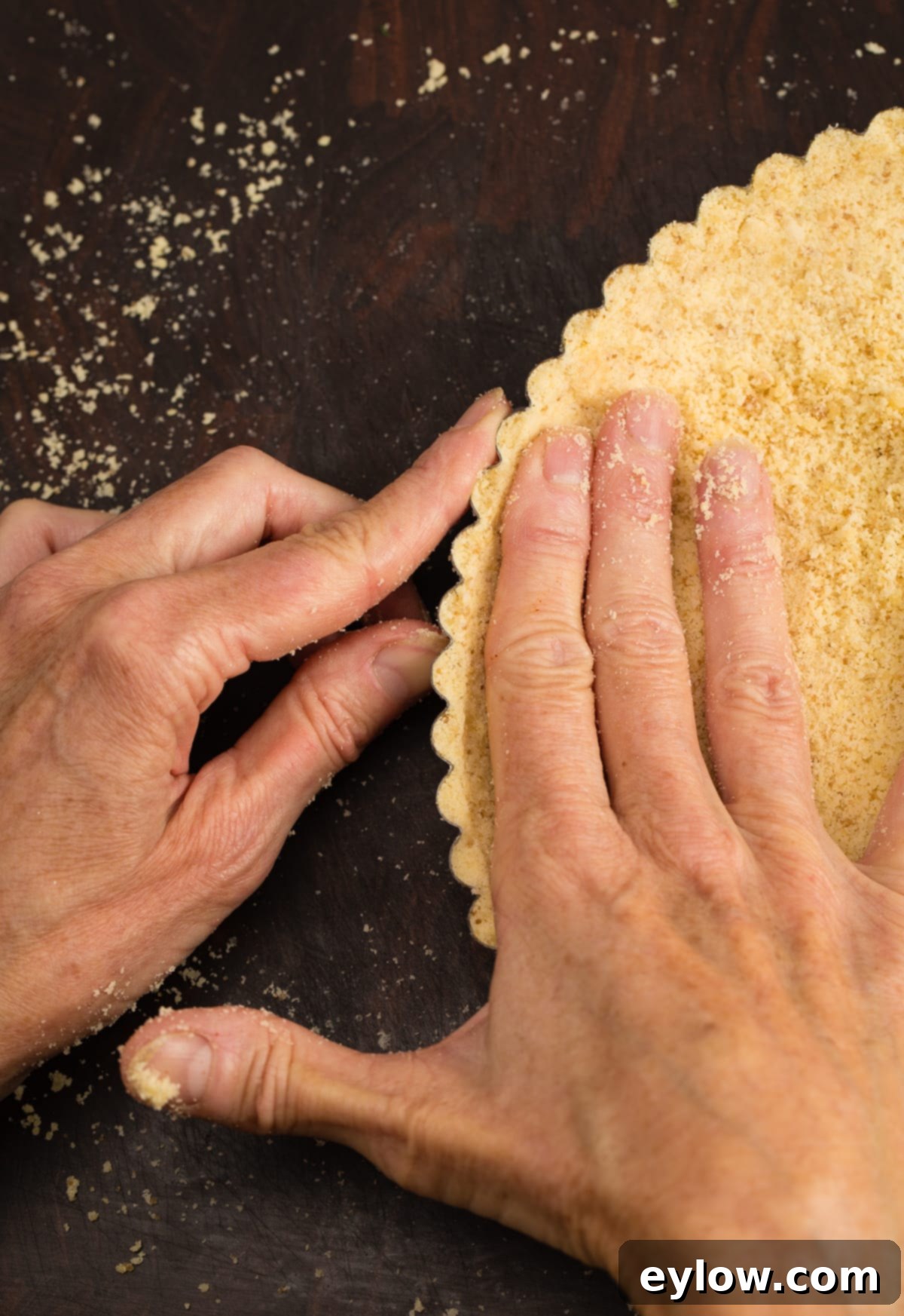 Hands carefully pressing and forming a gluten-free tart crust into the edges and base of a tart pan.