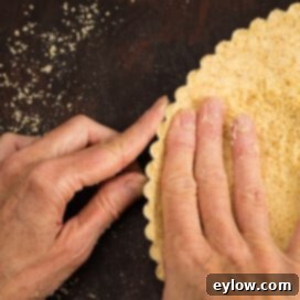 Hands forming a gluten-free almond and coconut tart crust, building up the edges in the tart pan.
