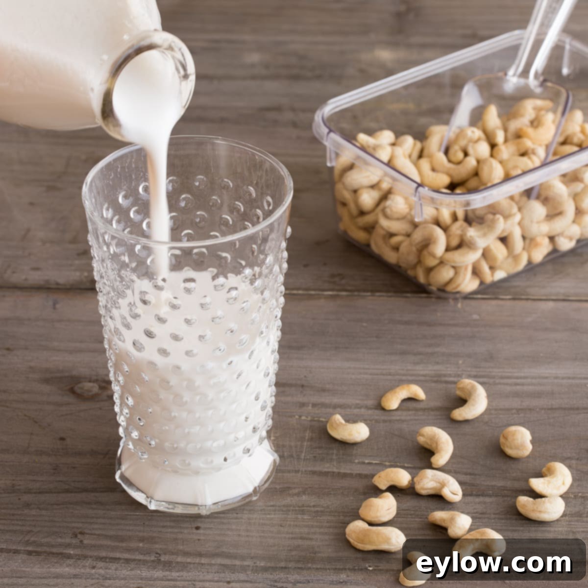Creamy Homemade Cashew Milk 2 Homemade cashew milk pouring into a glass on a wooden counter, highlighting its rich, creamy texture.
