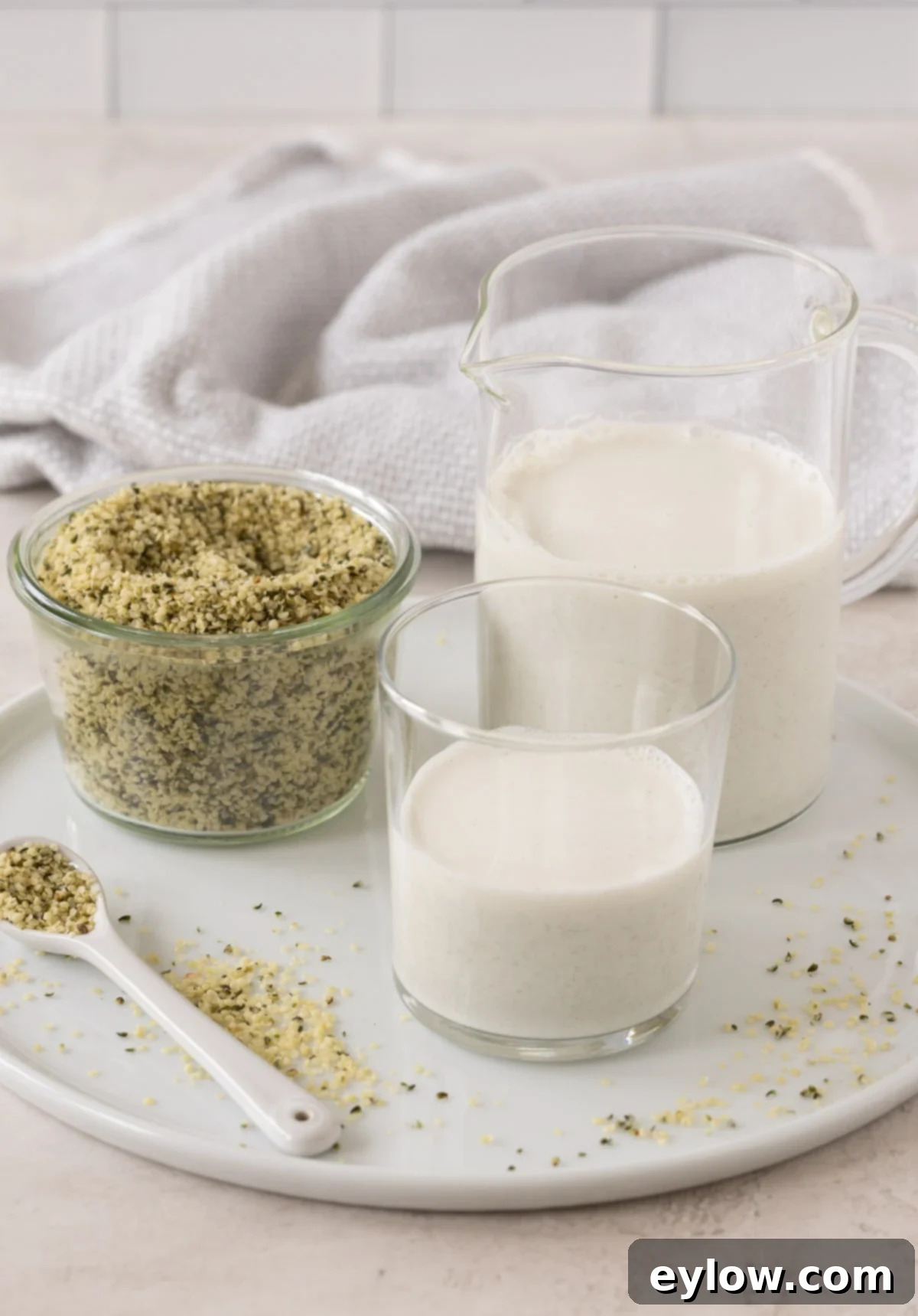 Creamy Homemade Hemp Mylk 2 White hemp milk in a glass and pitcher with seeds in a jar.