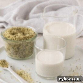 Creamy Homemade Hemp Mylk 8 White round platter with a glass of hemp seed milk, a pitcher, and hemp seeds.