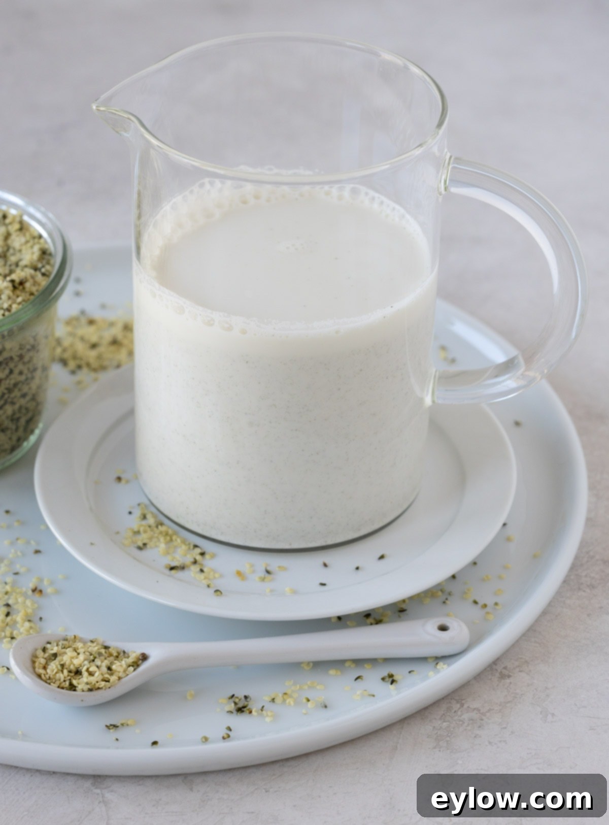 Creamy Homemade Hemp Mylk 7 Hemp seed milk n a glass pitcher on a tray with hemp seeds.