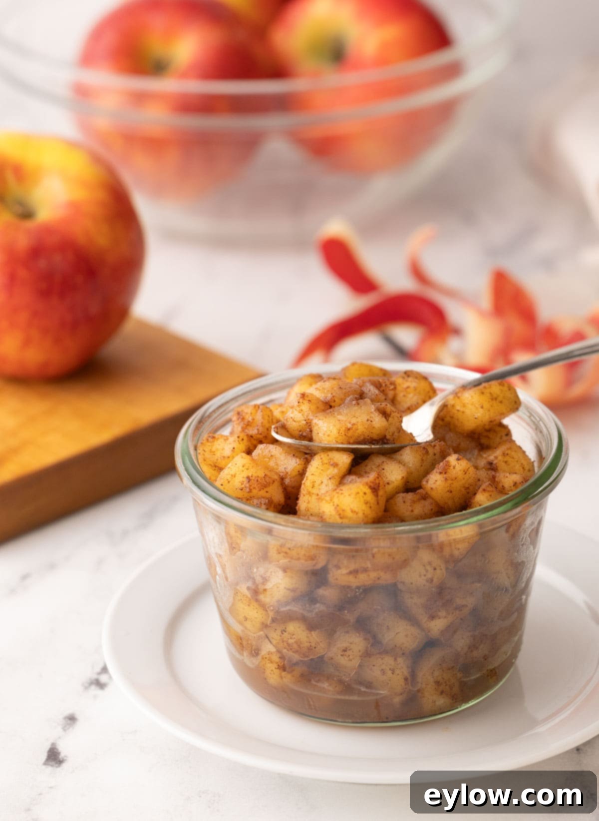 A jar of cinnamon apple compote with reddish gold apples behind.