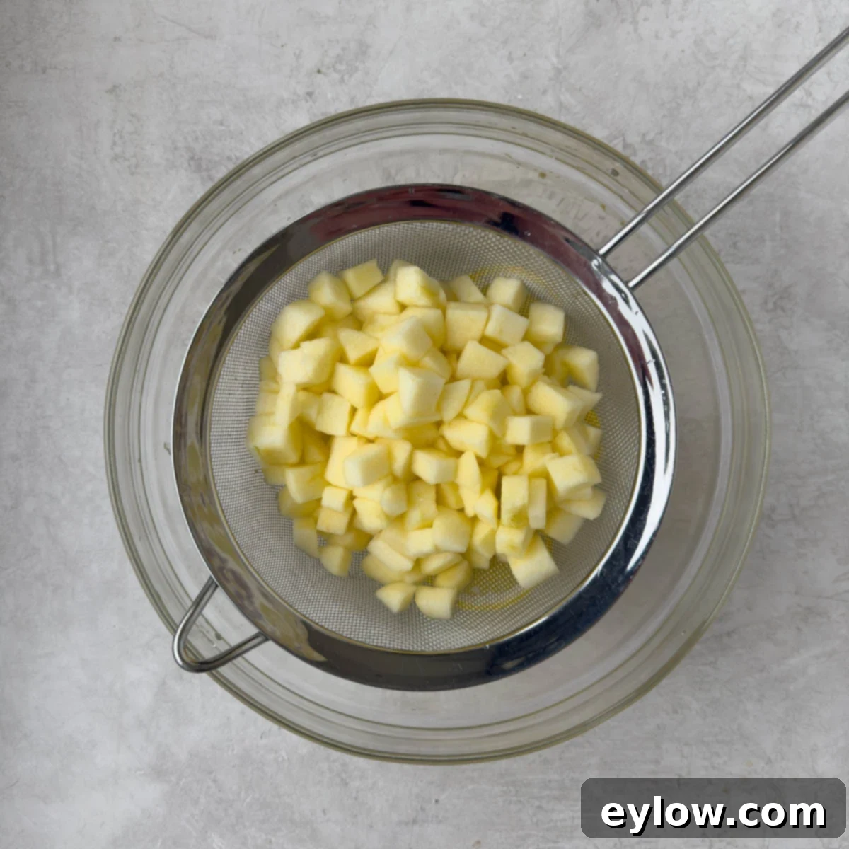 Apples draining in a sieve over a glass bowl.