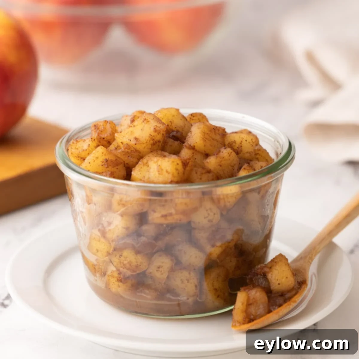 Closeup of a jar of cooked apple compote with spices and a spoon. 