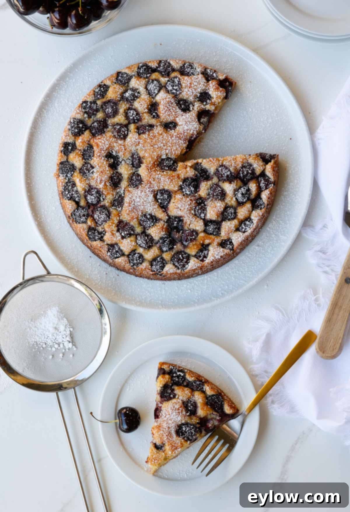 A sweet cherry cake on a white plate with a slice on a small plate.