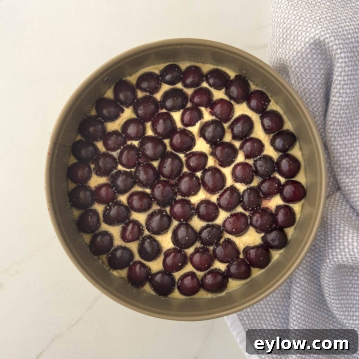 Cake batter topped with halved red cherries. 