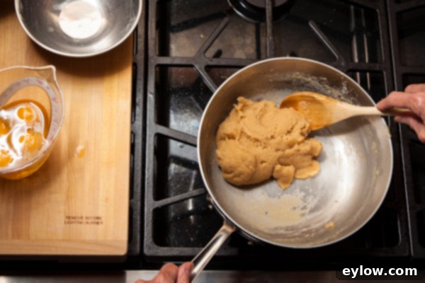 Gougere Cheese Puff-2236 Pate a choux dough in a stainless steel pan, almost finished, being stirred with a wooden spoon.