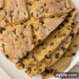 Golden baked loaf of Irish soda bread, sliced on a white plate.