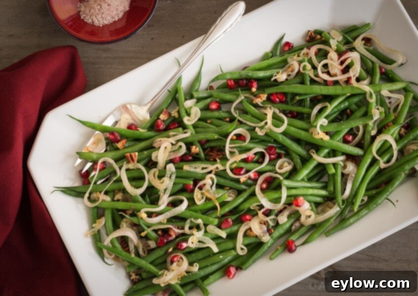 Thanksgiving's Easiest Green Beans 2 Green beans on a platter with shallots and pomegranate seeds.