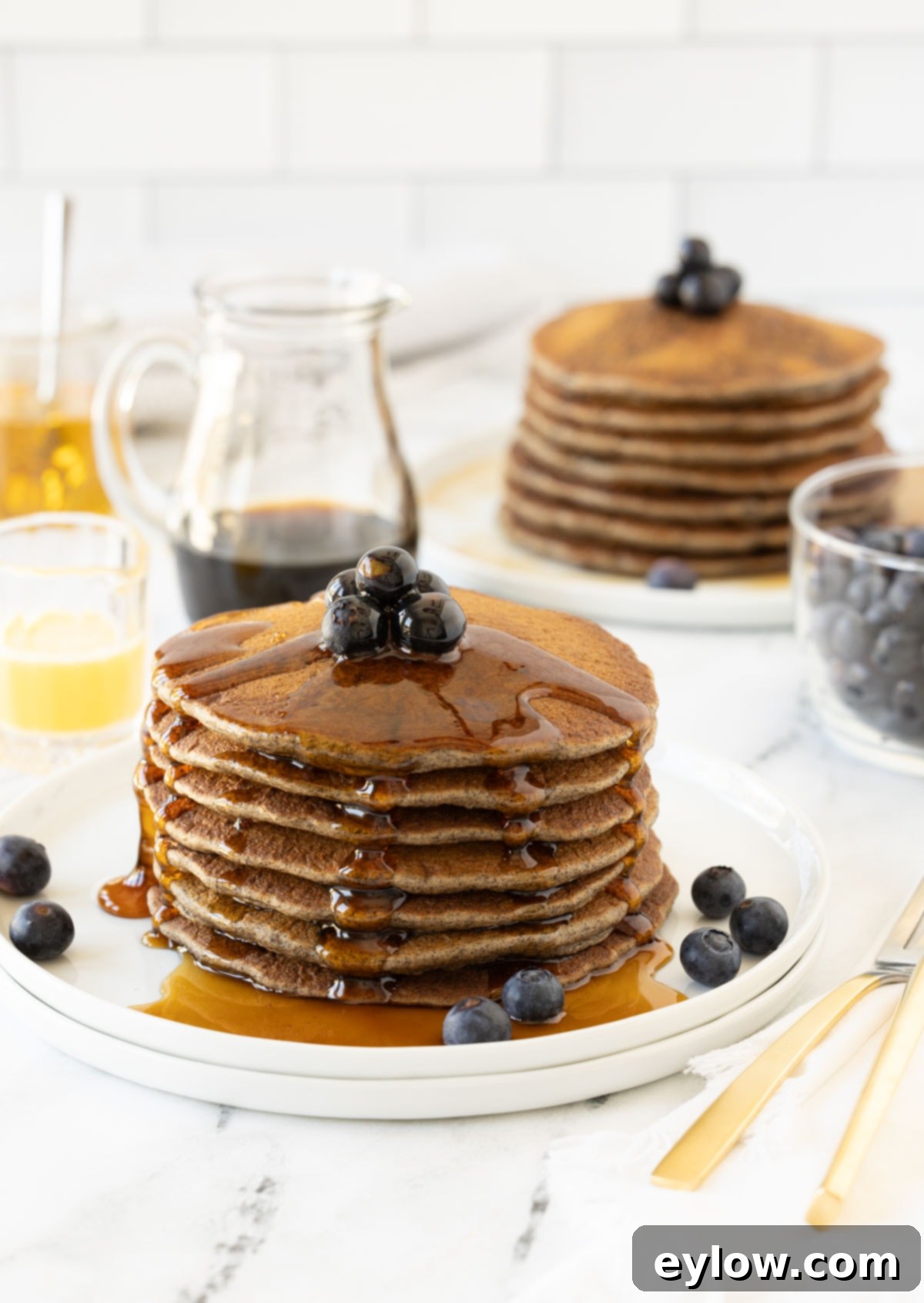 A big stack of golden-brown buttermilk buckwheat pancakes, generously dripping with rich maple syrup and garnished with fresh berries.