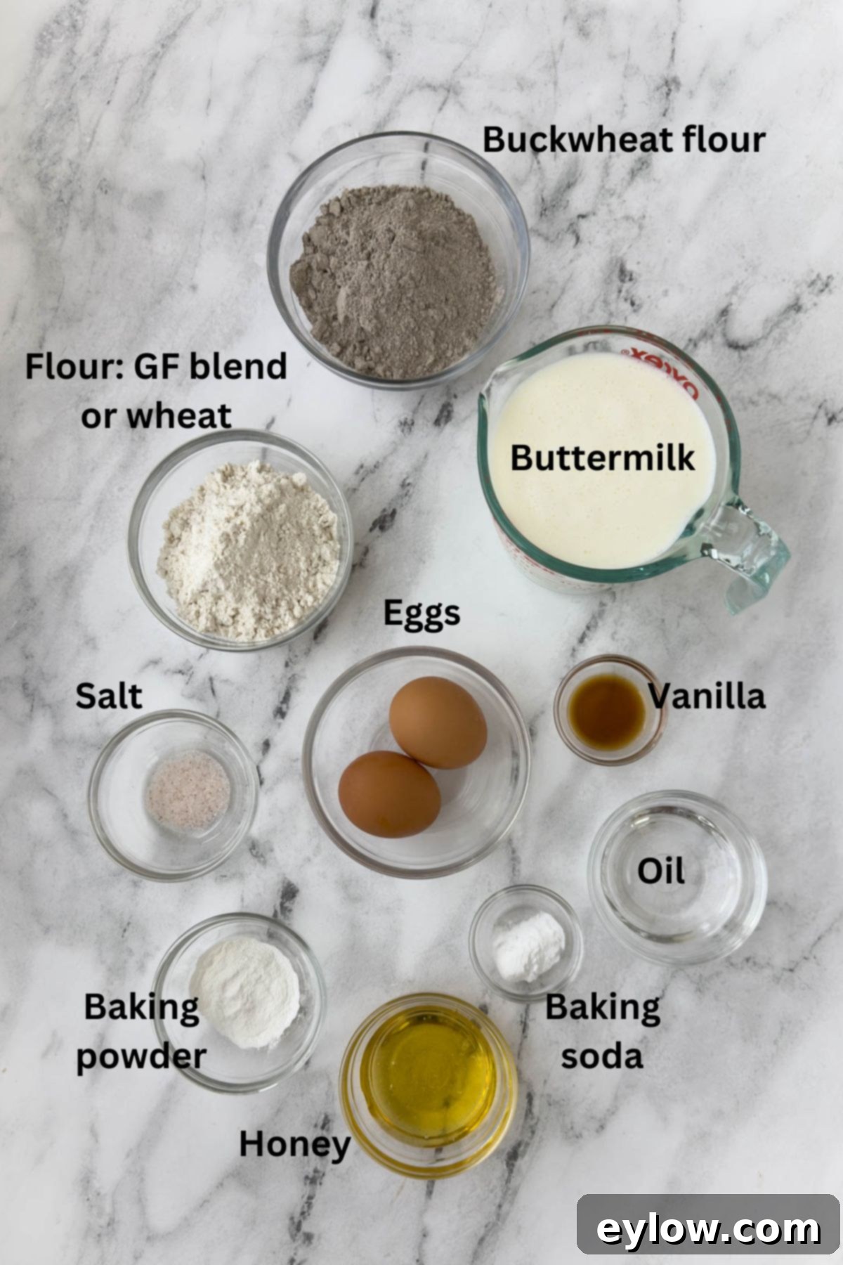 Various ingredients for buckwheat pancakes laid out in small bowls, including flours, eggs, and liquids, ready for mixing the batter.