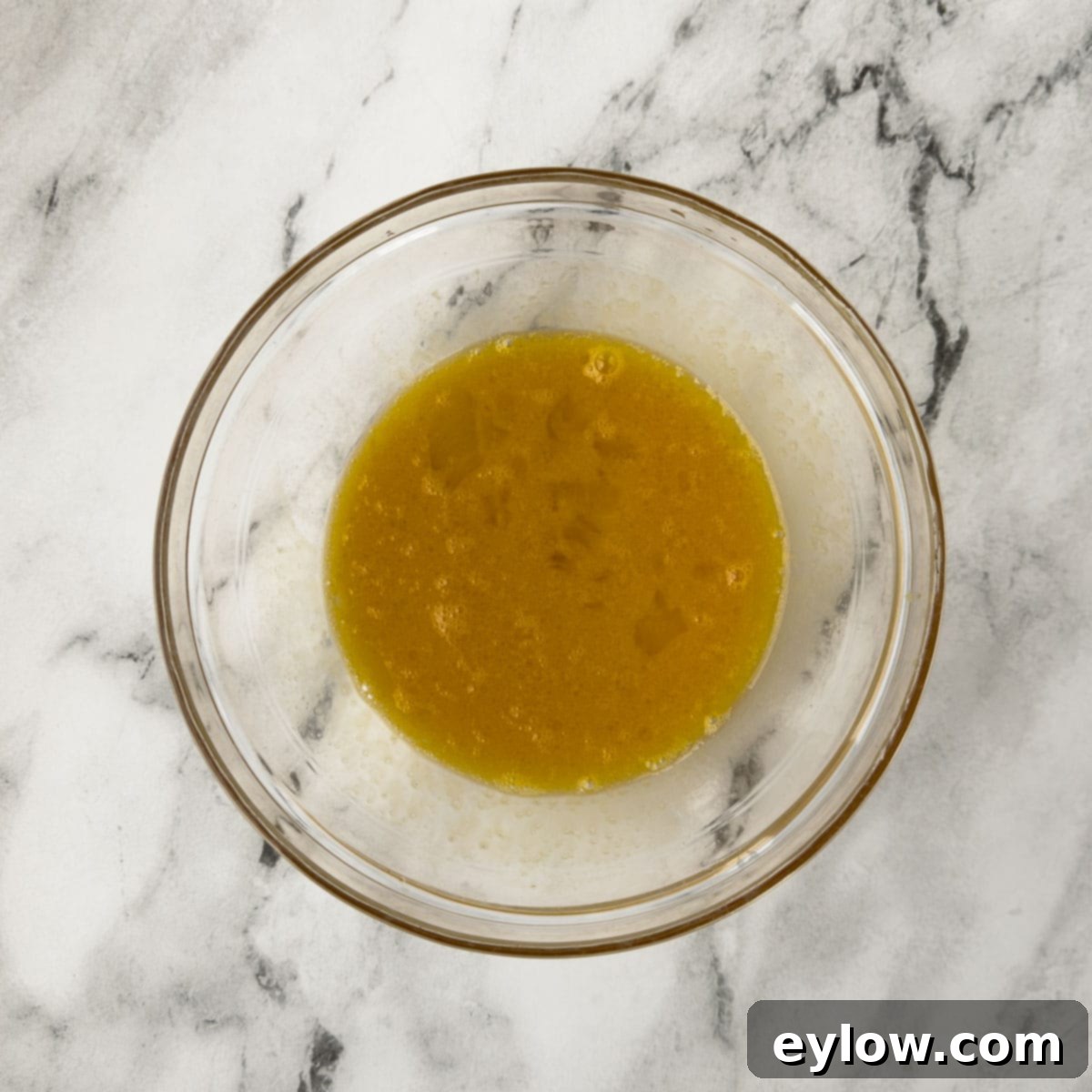 Fresh eggs, healthy oil, and golden honey are vigorously whisked together in a clean glass mixing bowl, forming the base of the wet ingredients.