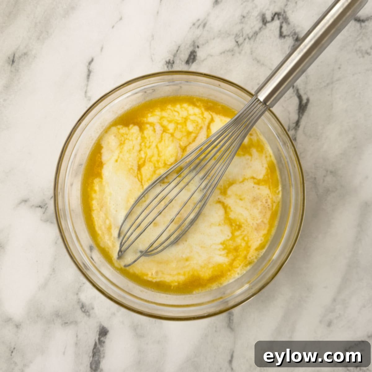 Pancake batter is gently mixed with a whisk in a large bowl, showing the consistency of the combined wet and dry ingredients before cooking.