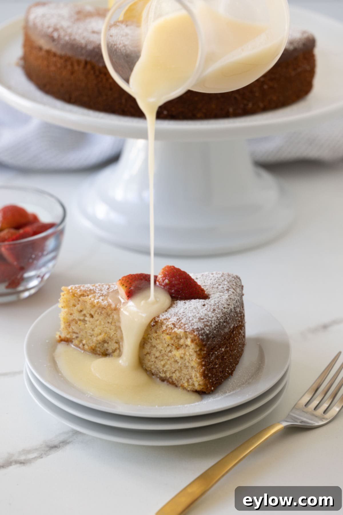 A slice of lemon olive oil cake drizzled with lemon glaze, the cake behind.