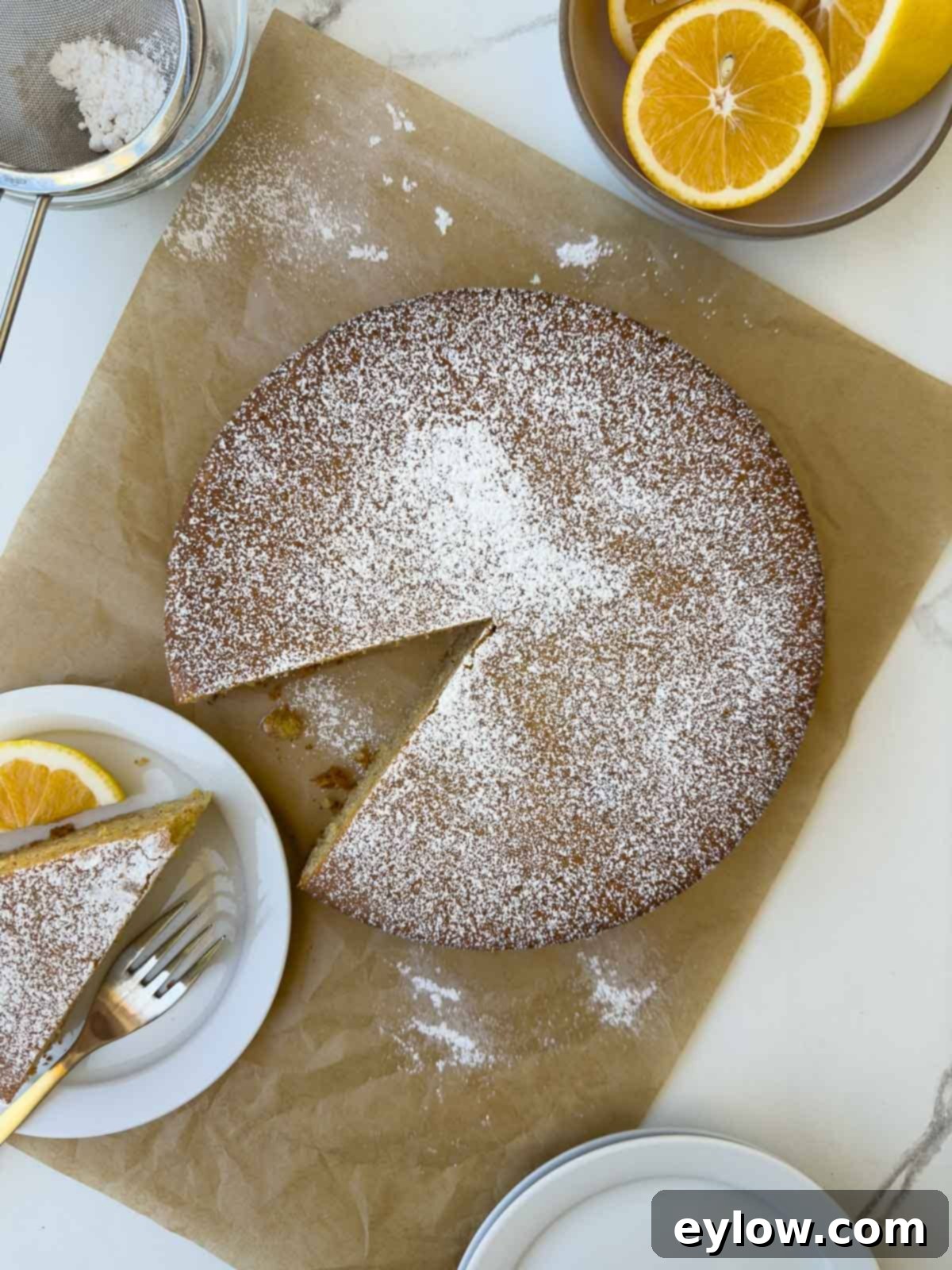 Top down view of a baked olive oil cake sifted with powdered sugar on parchment paper.
