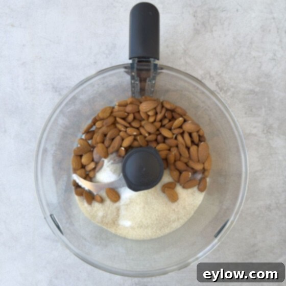 Whole almonds and sugar in the bowl of a food processor. 