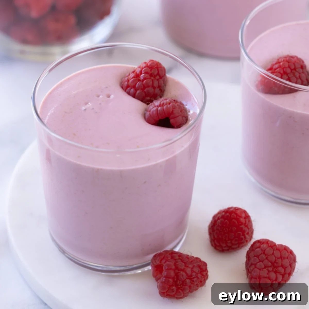 A bright pink berry smoothie with fresh raspberries inside the glass.