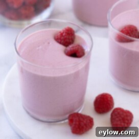 A bright pink berry smoothie with fresh raspberries inside the glass.