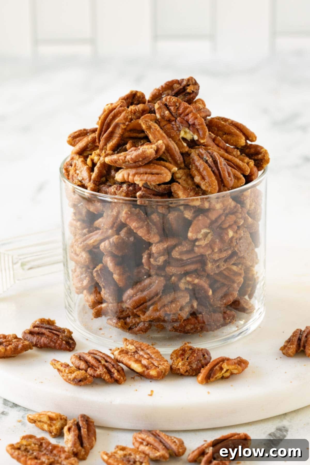 A glass jar overflowing with golden brown candied pecans on a marble counter, ready to be enjoyed or gifted.