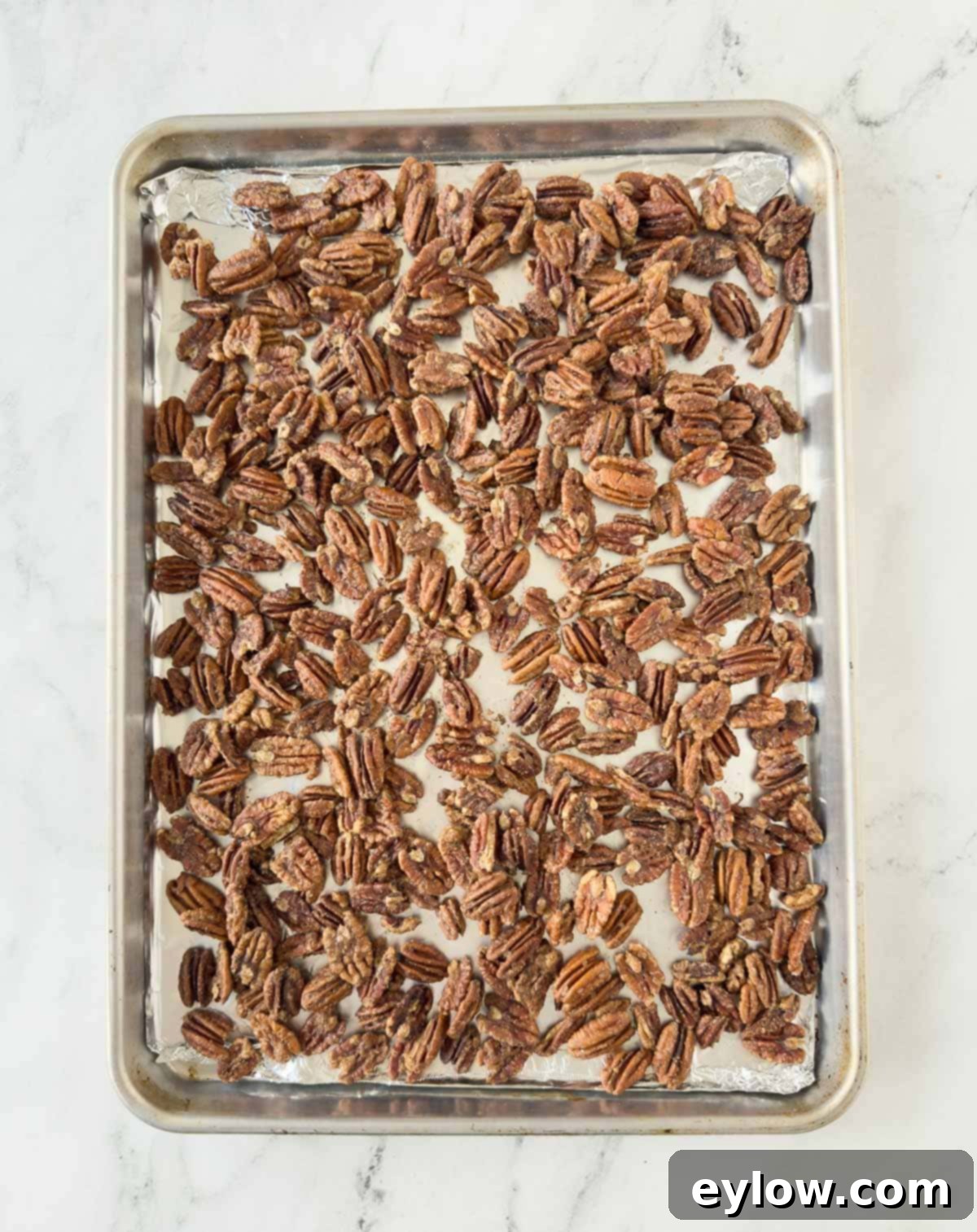 An aluminum foil covered baking sheet of baked candied pecans cooling on a wire rack.