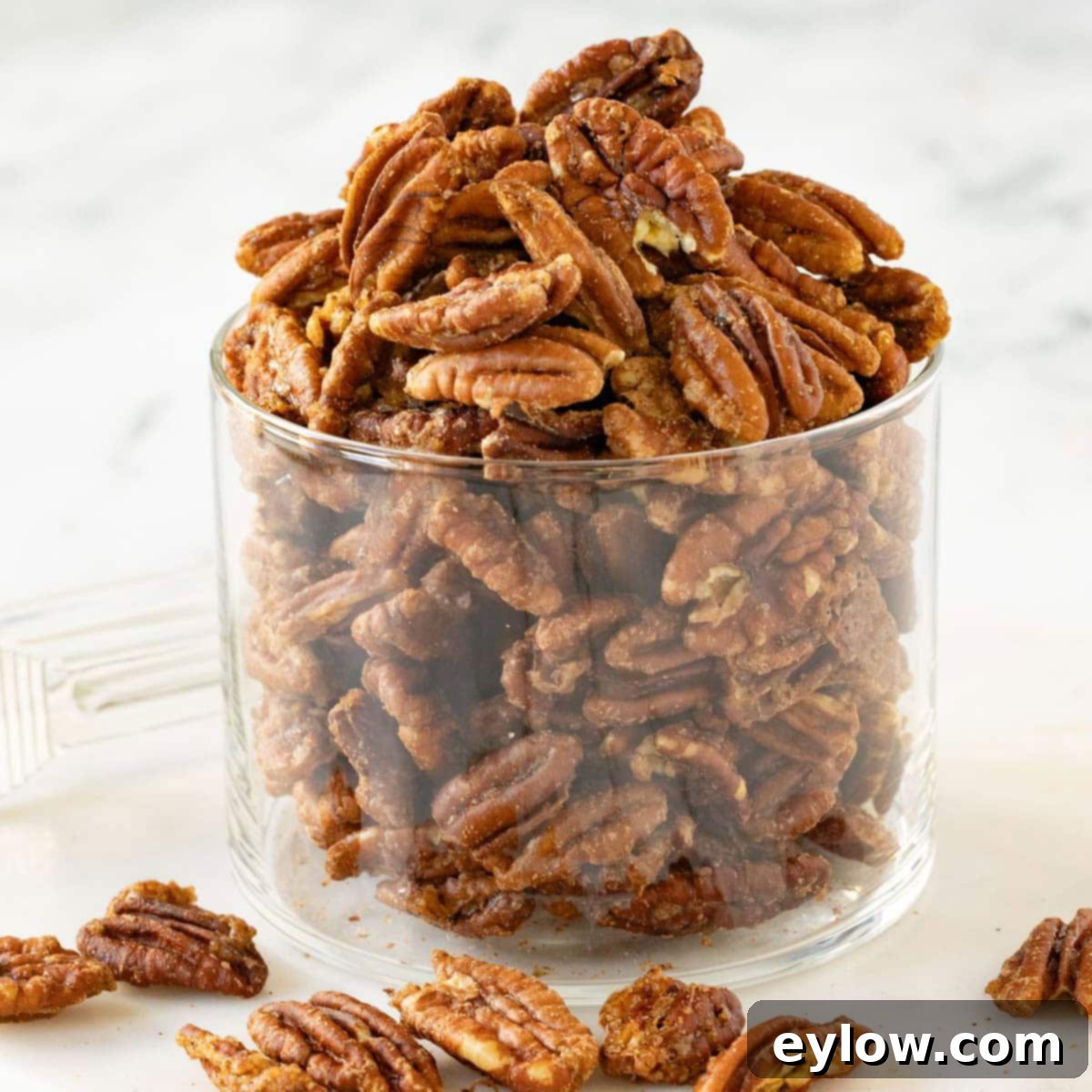 A jar of golden glazed pecans on a white round marble plate, showcasing their perfect coating.