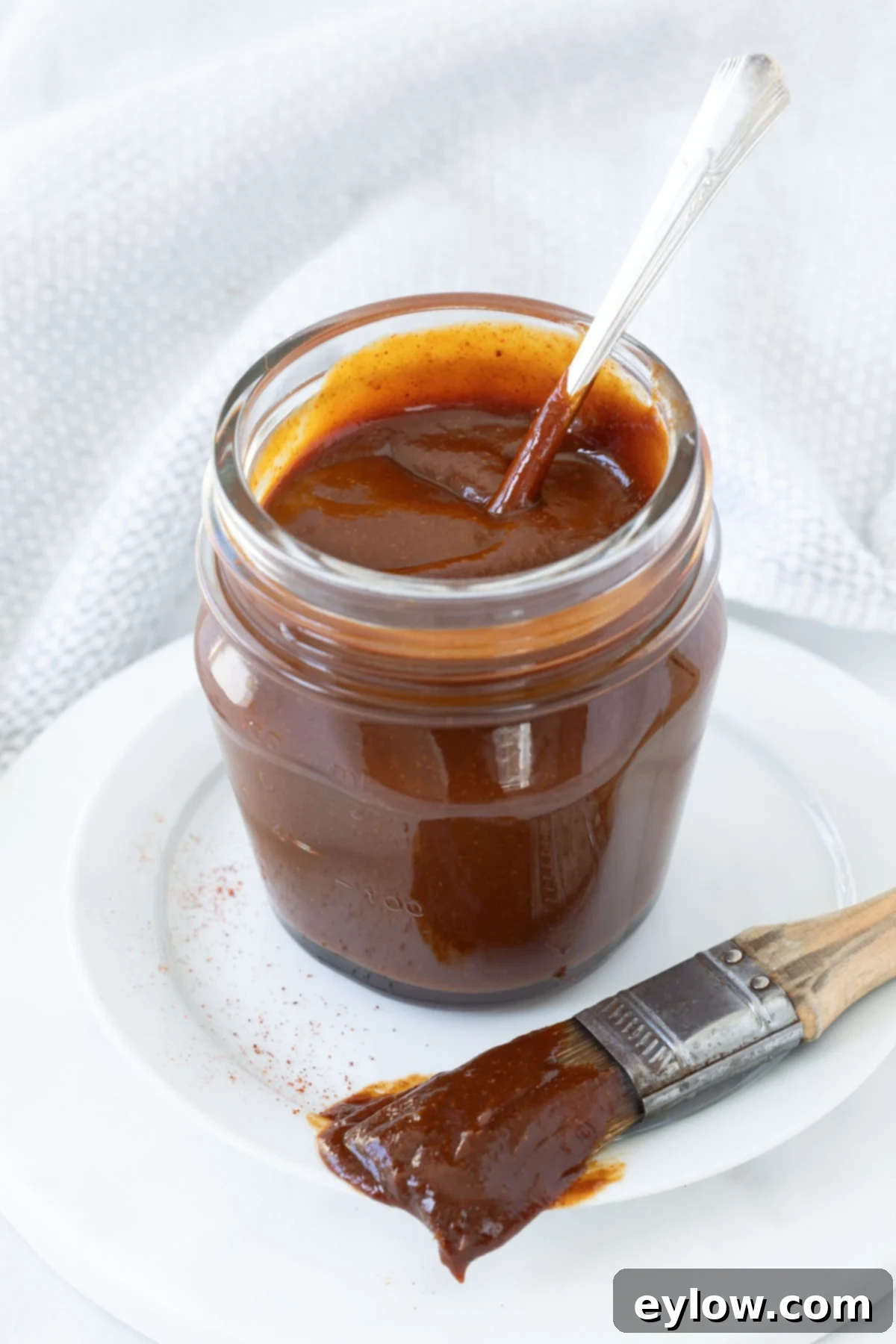 A jar of burnished red, thick homemade bbq  sauce with a pastry brush. 