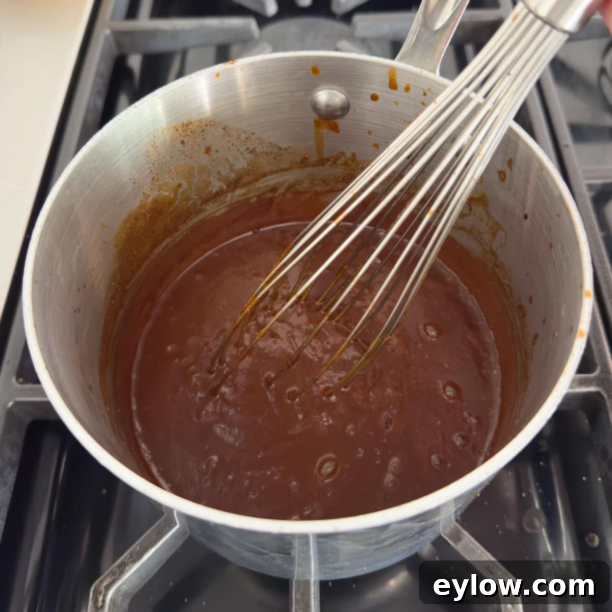 Whisking bbq sauce in a small stainless steel pan to thicken.