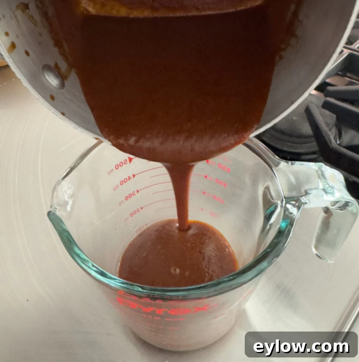Pouring finished barbecue sauce from pan into a glass measuring cup.