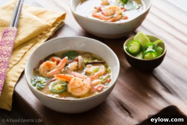 A close-up of a vibrant Tom Yum shrimp soup with clear broth, featuring plump shrimp, sliced mushrooms, green snow peas, and red tomato wedges, ready to be served.