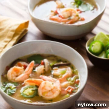 A bowl of Tom Yum Thai Soup with Shrimp, garnished with fresh cilantro and a lime wedge, sitting on a rustic wooden surface, inviting you to savor its flavors.