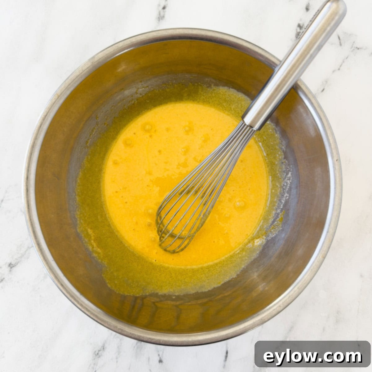 Aromatic Vanilla Bean Bliss 5 Bright yellow whisked egg yolks with sugar, and a silver whisk.