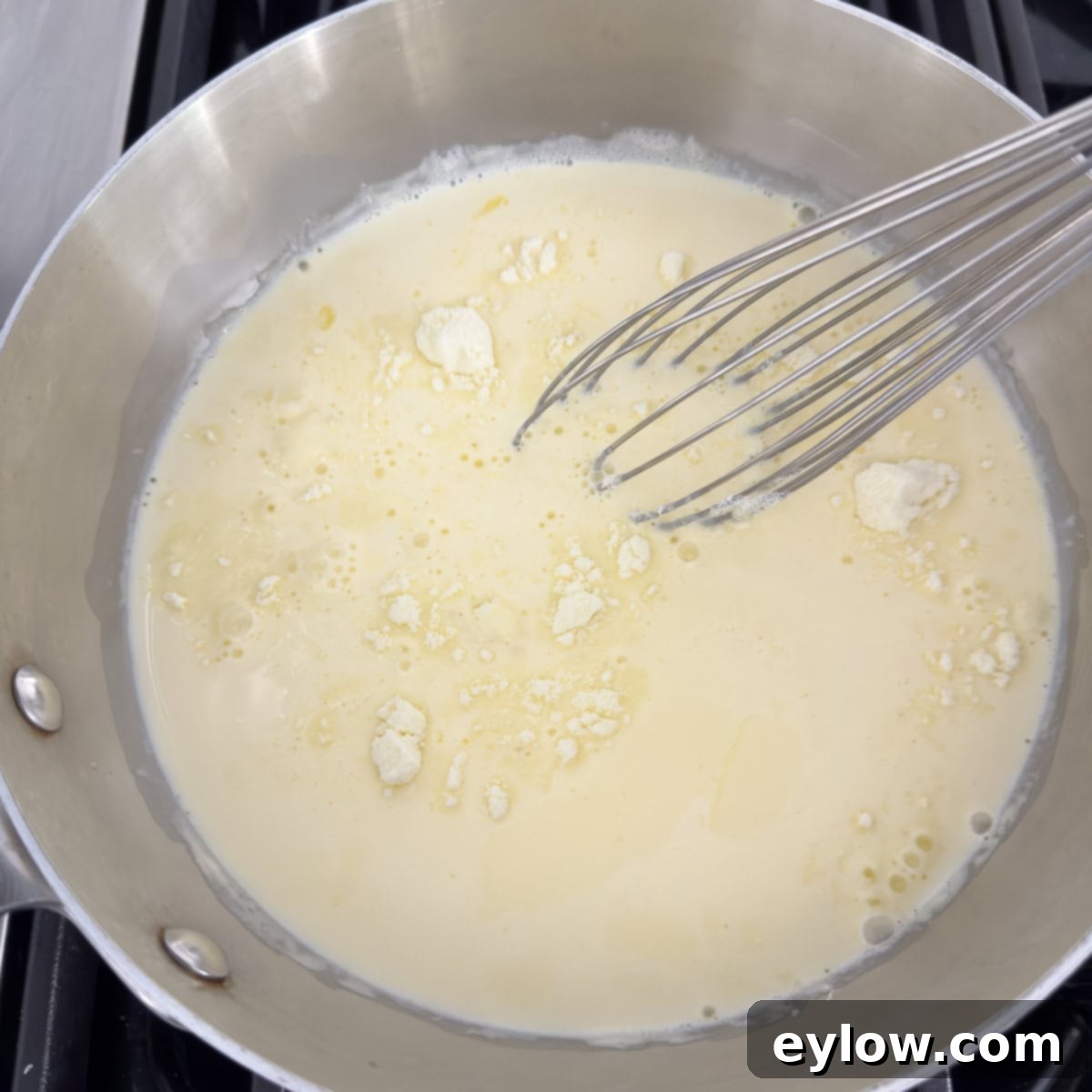 Aromatic Vanilla Bean Bliss 6 A stainless steel pan with heavy cream and milk powder, and a whisk.