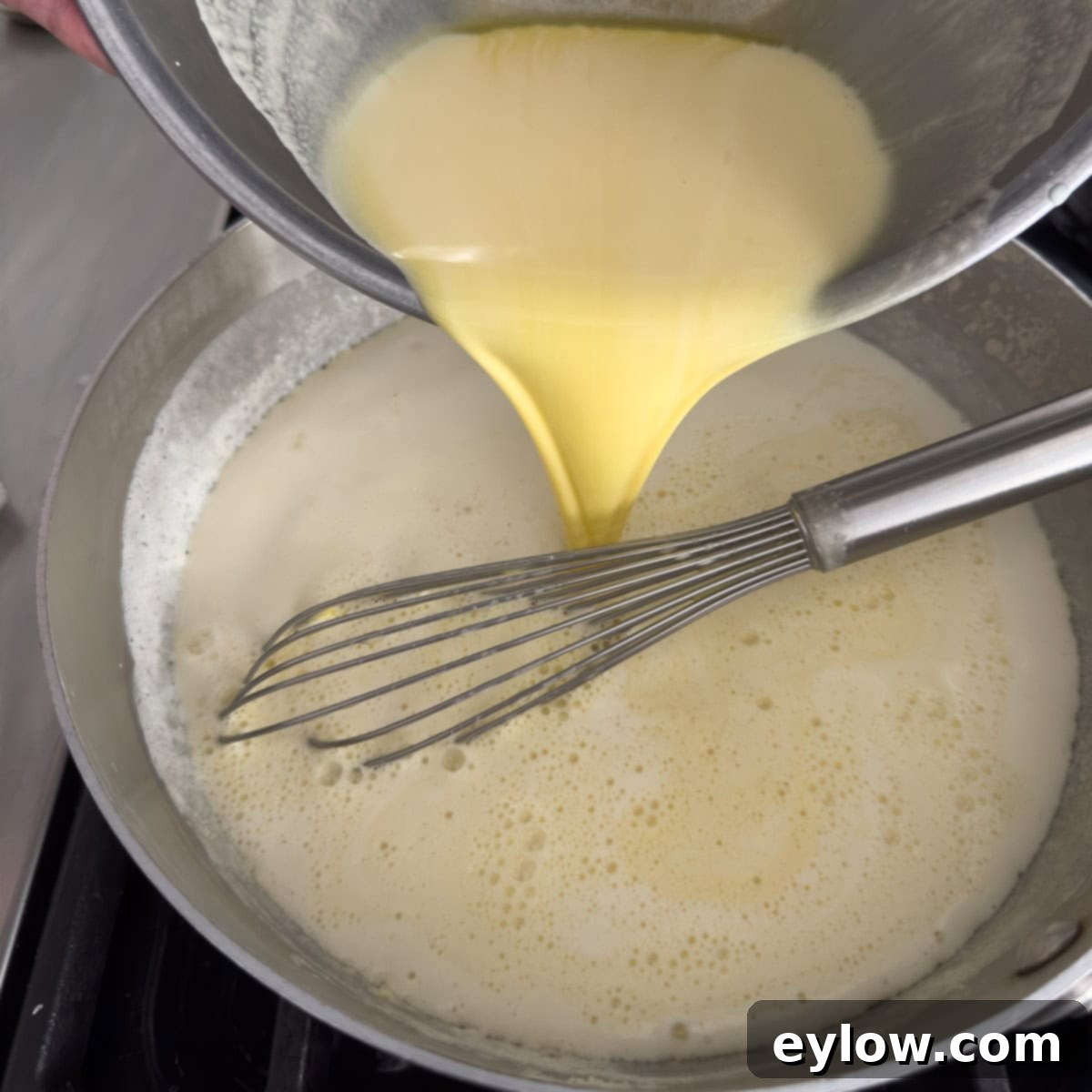 Aromatic Vanilla Bean Bliss 7 Pouring cooked egg yolks and cream into a stainless steel pan for cooking an ice cream base.