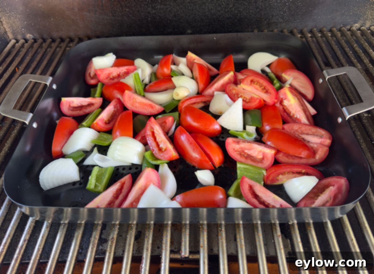 A black grill basket filled with tomatoes, onions, garlic and peppers for smoked salsa.