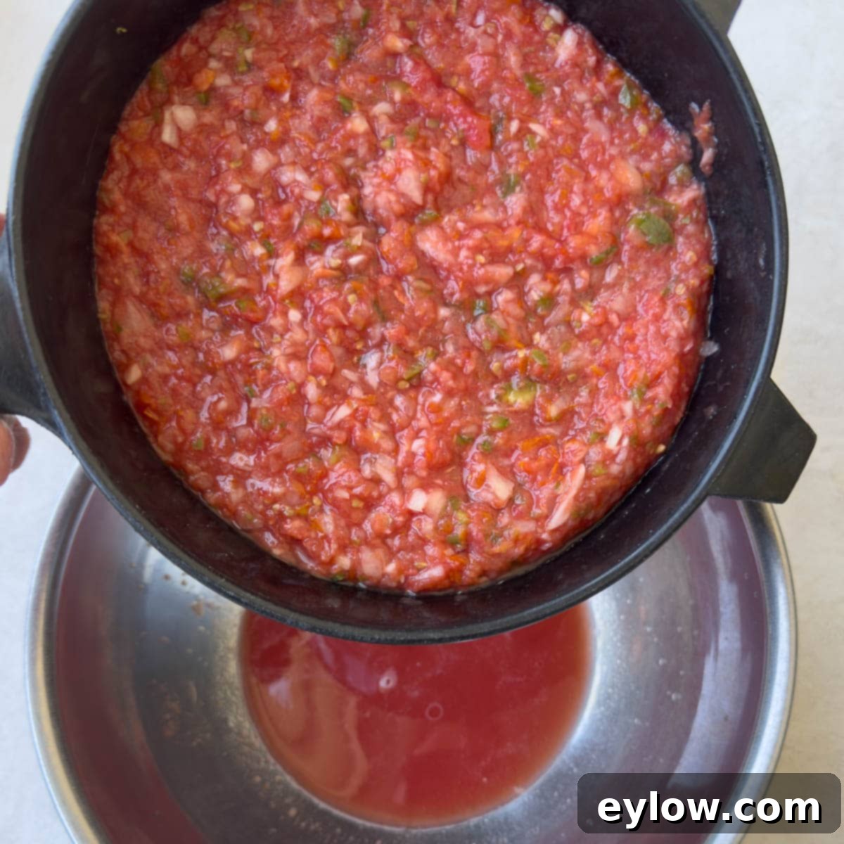 Straining smoked tomato salsa from sieve into a bowl.