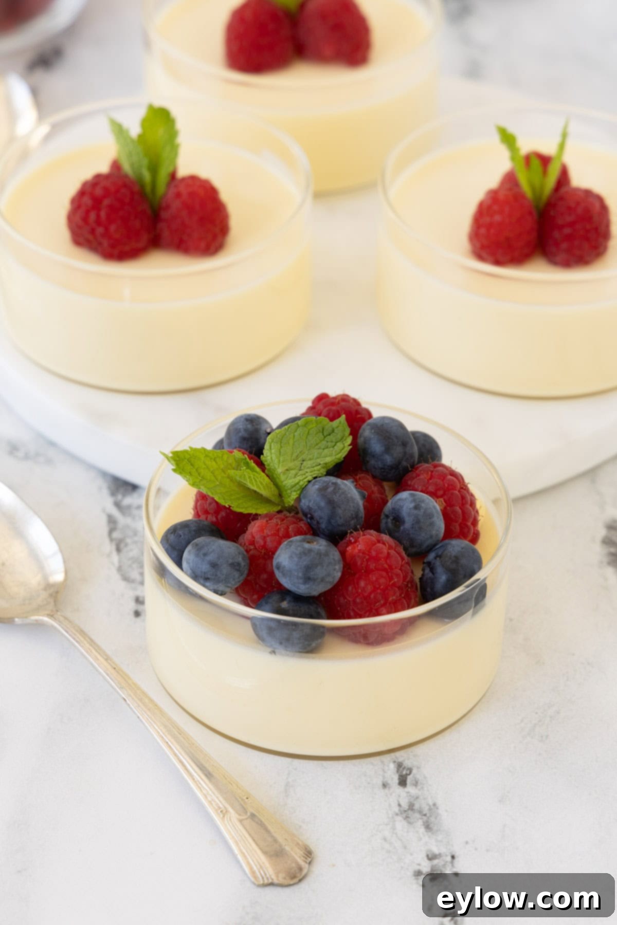 Simply Divine Lemon Posset 2 Pale lemon colored lemon possets in glass cups topped with raspberries and blueberries.