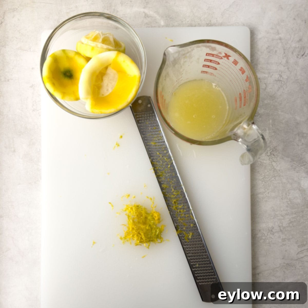 Simply Divine Lemon Posset 4 Lemons being juice and zested on a white cutting board with a microplane zester.