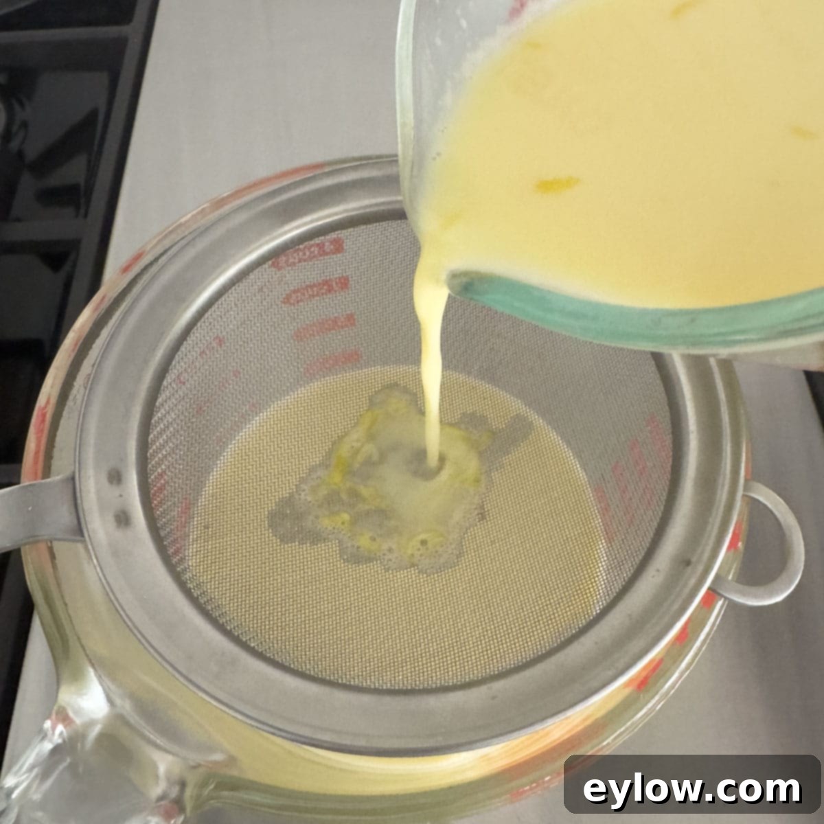 Simply Divine Lemon Posset 6 Straining lemon zest through a fine sieve into a large glass measuring cup.
