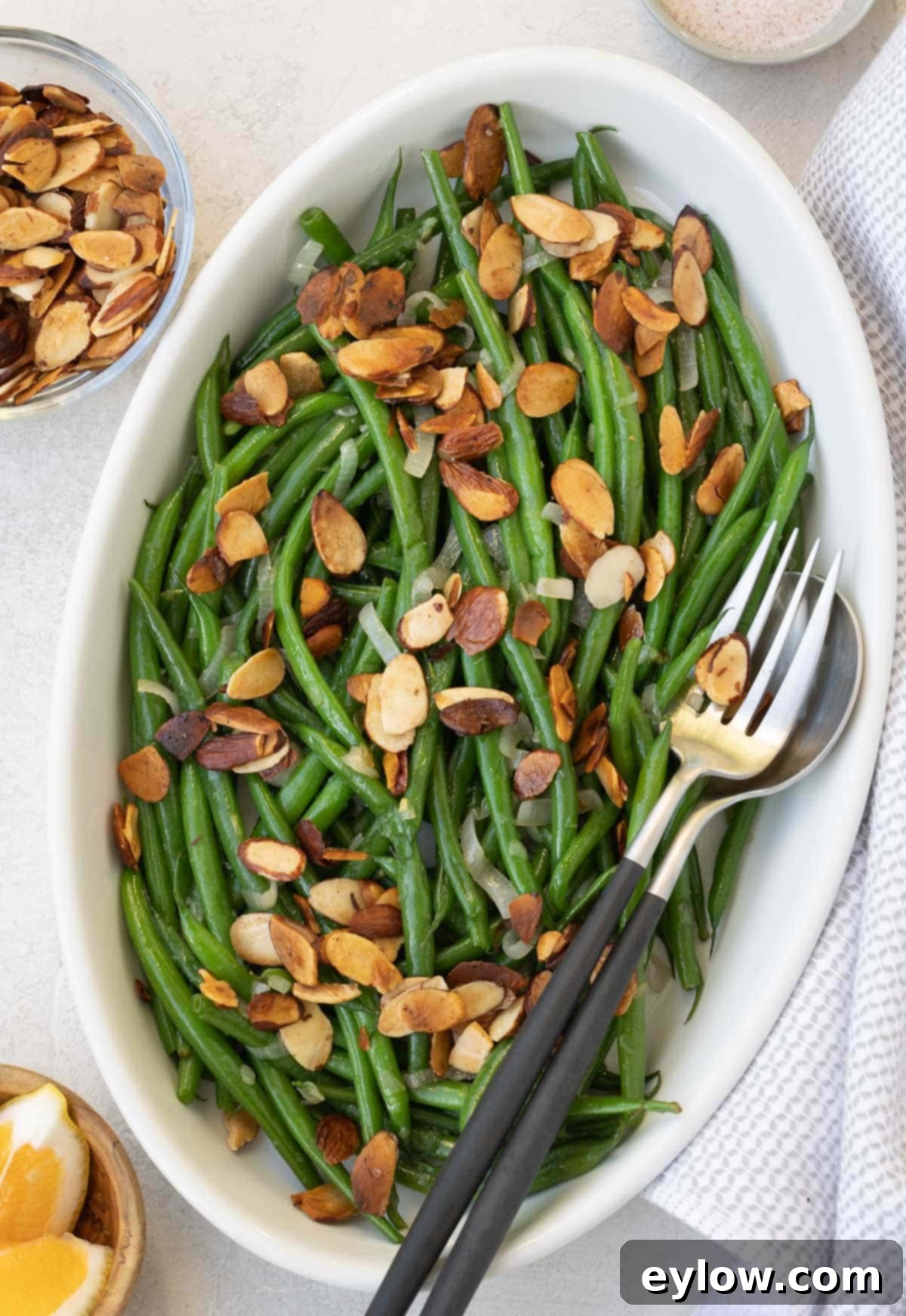 Green beans almondine in a shallow oval bowl scattered with toasted almonds.