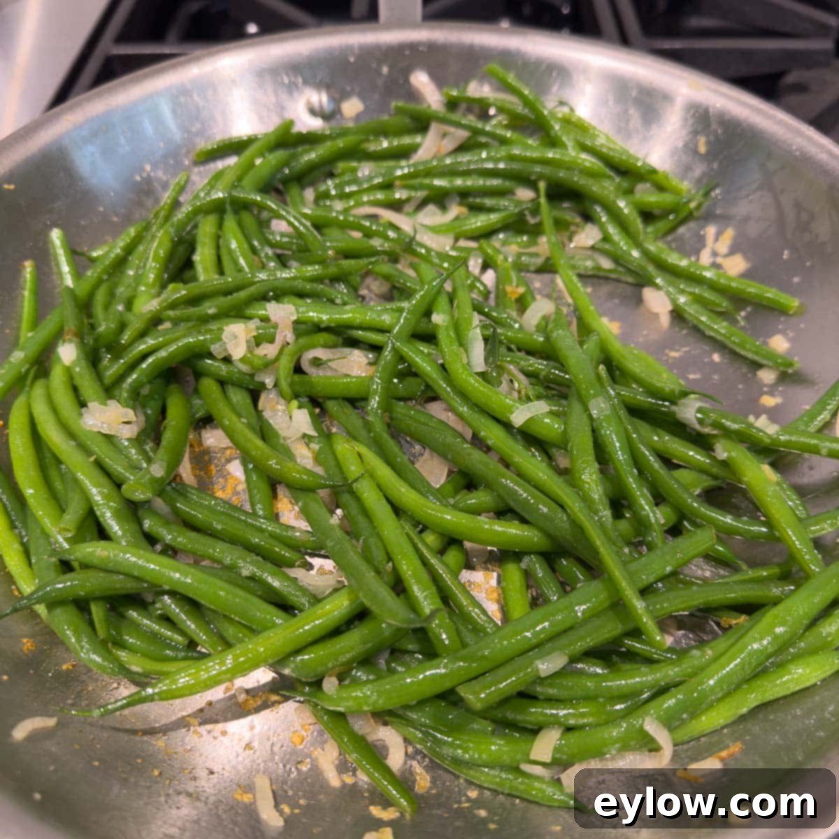Adding green beans to the shallots to heat up for serving.