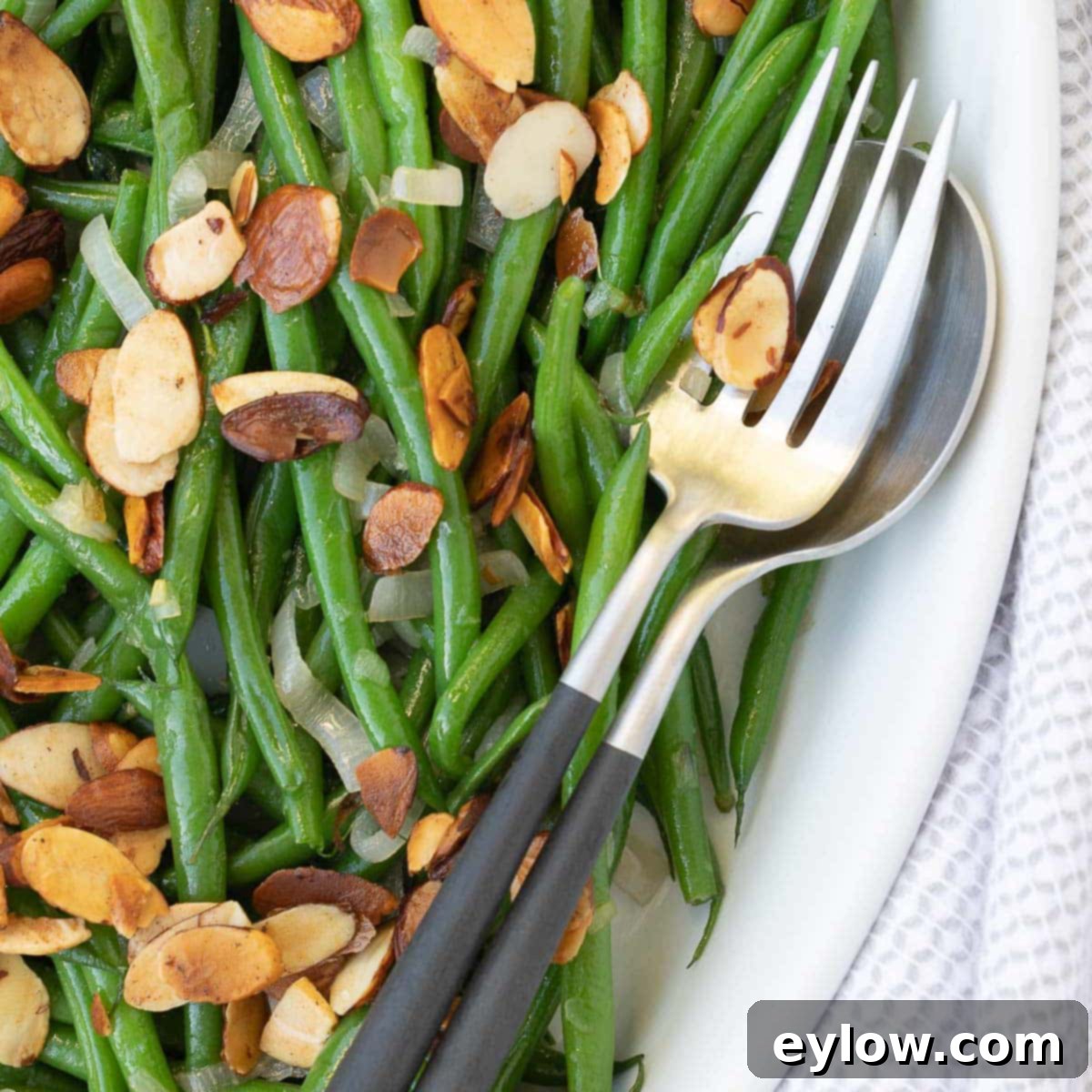 A bowl of bright green beans with toasted buttered almonds.