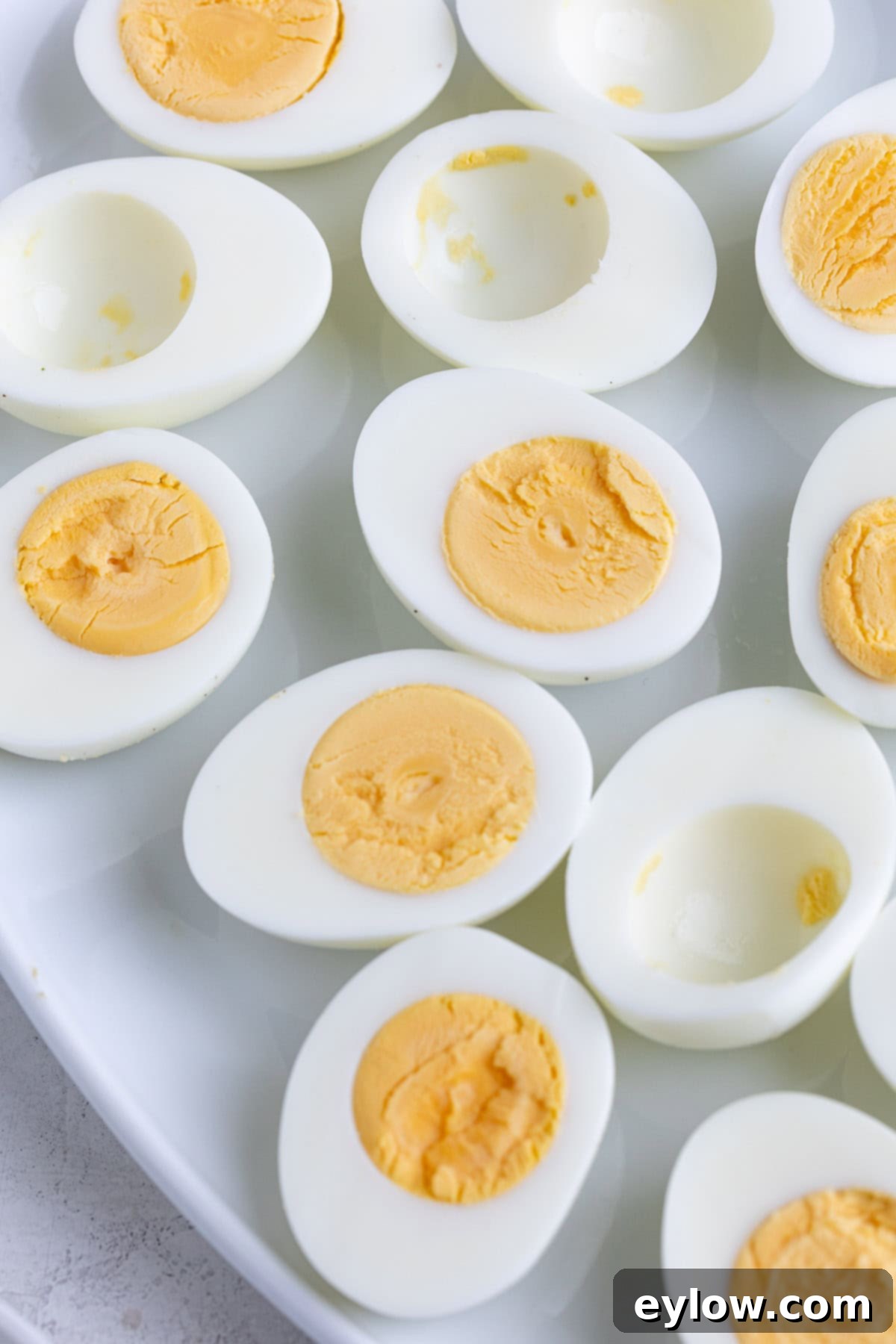 Flawless Hard Boiled Eggs That Peel Effortlessly 4 Hard-boiled eggs cut in half on a white plate, showcasing creamy yolks without a green ring.