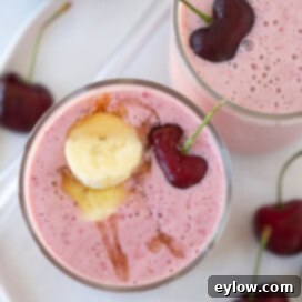 Easy 5-Minute Cherry Smoothie 9 A beautifully presented, deep pink cherry smoothie in a tall glass, garnished with a banana slice and a fresh cherry, seen from a top-down perspective.