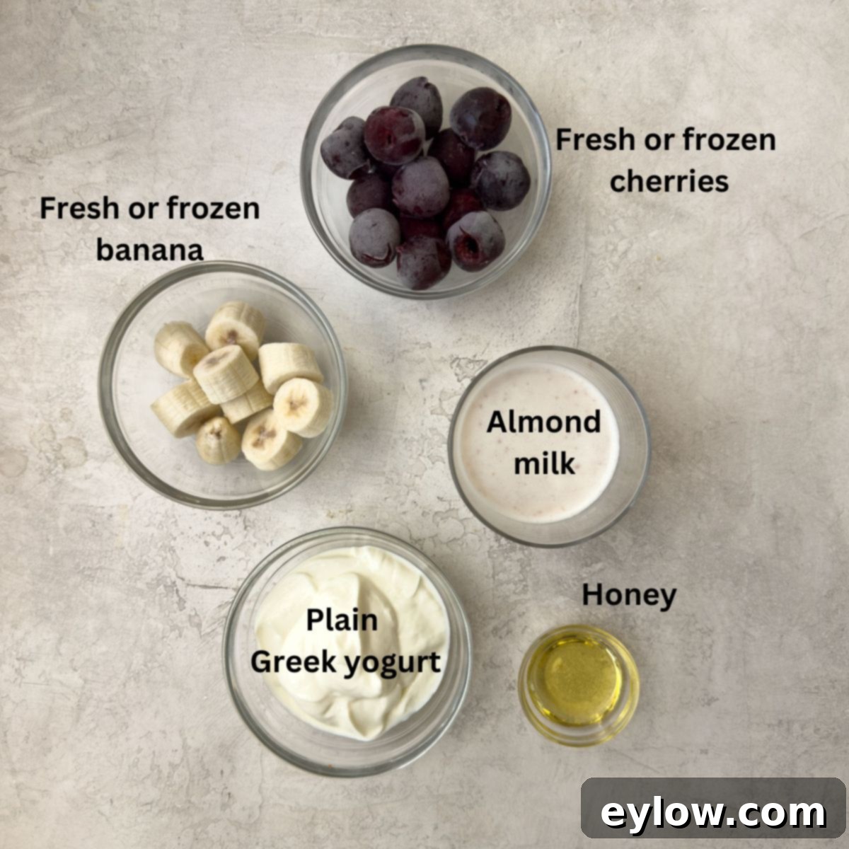 Easy 5-Minute Cherry Smoothie 3 Simple ingredients for a healthy cherry smoothie laid out in glass bowls, including milk, fresh cherries, Greek yogurt, banana, and honey.