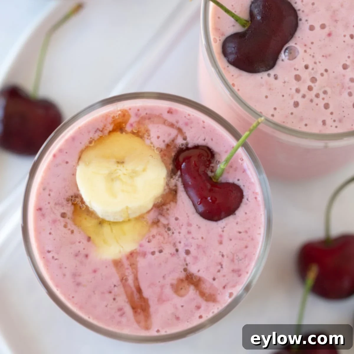 Easy 5-Minute Cherry Smoothie 8 Top-down view of a deep pink cherry smoothie in a tall glass, garnished with a banana slice and a fresh cherry.