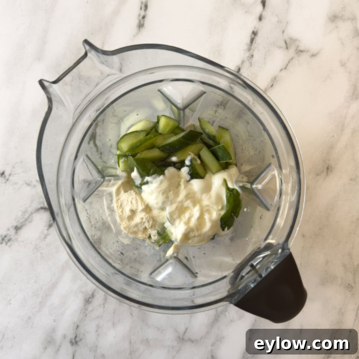 All ingredients for a cucumber smoothie layered in a high-speed blender container, ready to be blended.