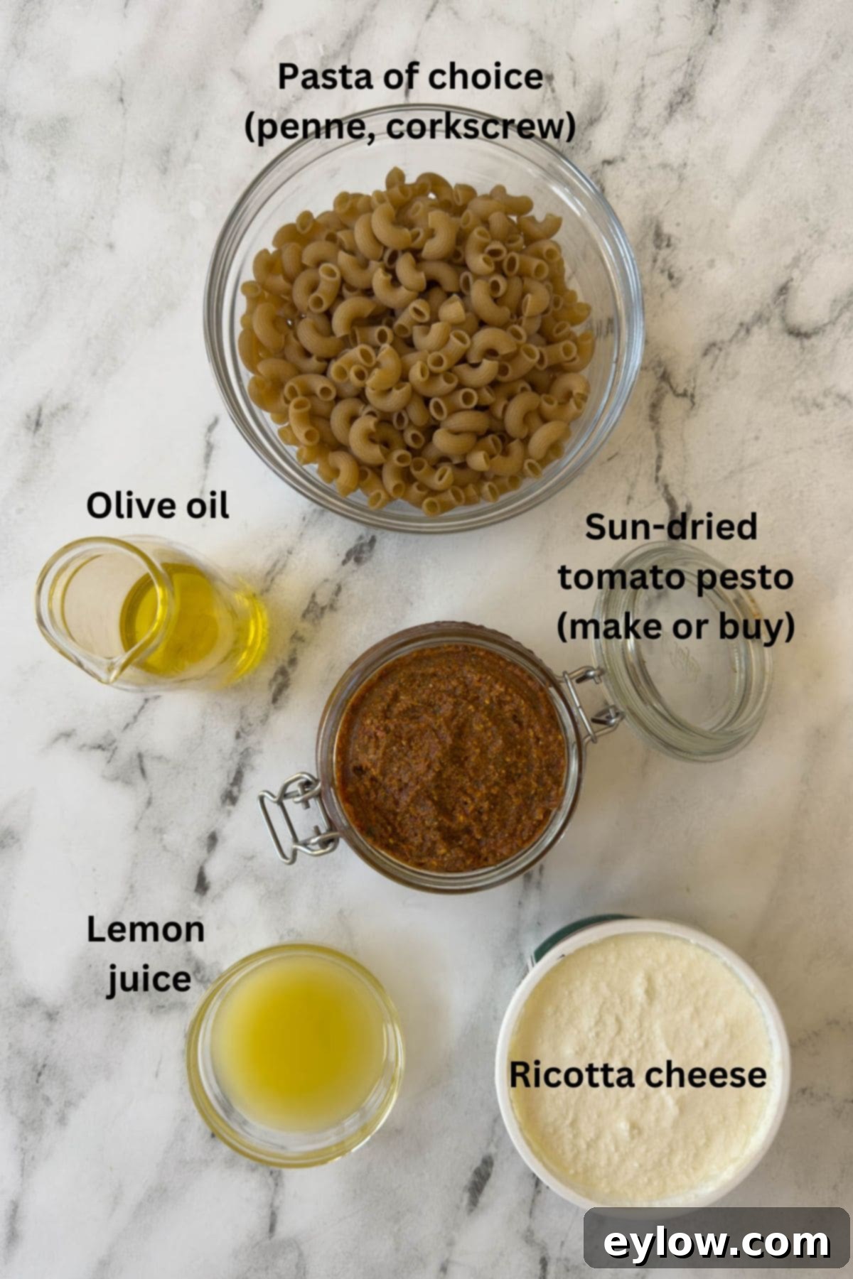 Velvety Sun-Dried Tomato Pesto Pasta 3 Ingredients for red pesto pasta on a marble counter with a bowl of cooked pasta.