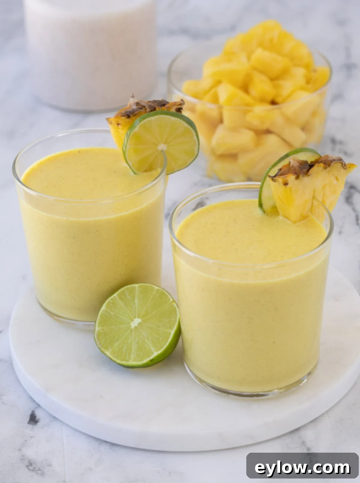 Two glasses of bright golden mango pineapple smoothies with lime and pineapple wedges.